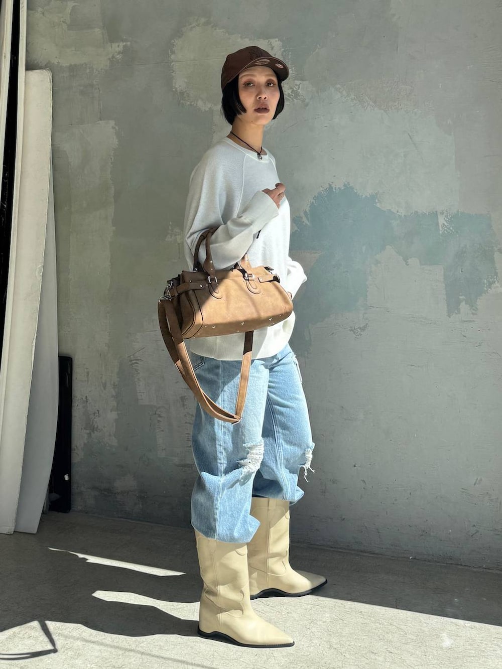 ブルー系のデニムパンツ、ホワイト系のブーツ、ブラウン系のボストンバッグを着用したレディースの秋コーディネートの3枚目の写真