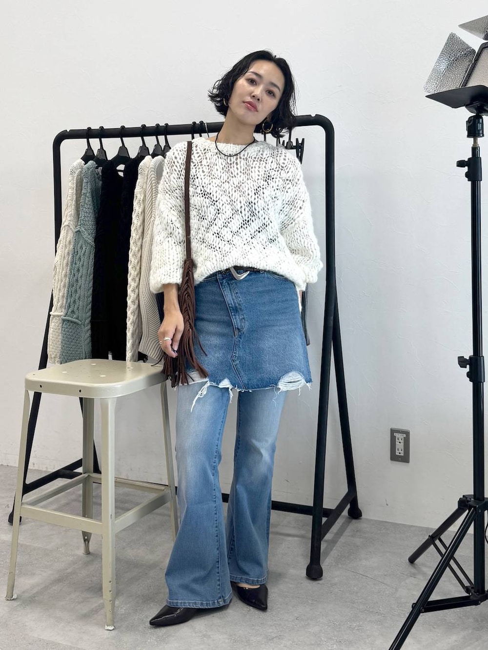 ブラウン系のショルダーバッグ、ブルー系のデニムスカート、ホワイト系のニット/セーターを着用したレディースの秋コーディネートの5枚目の写真