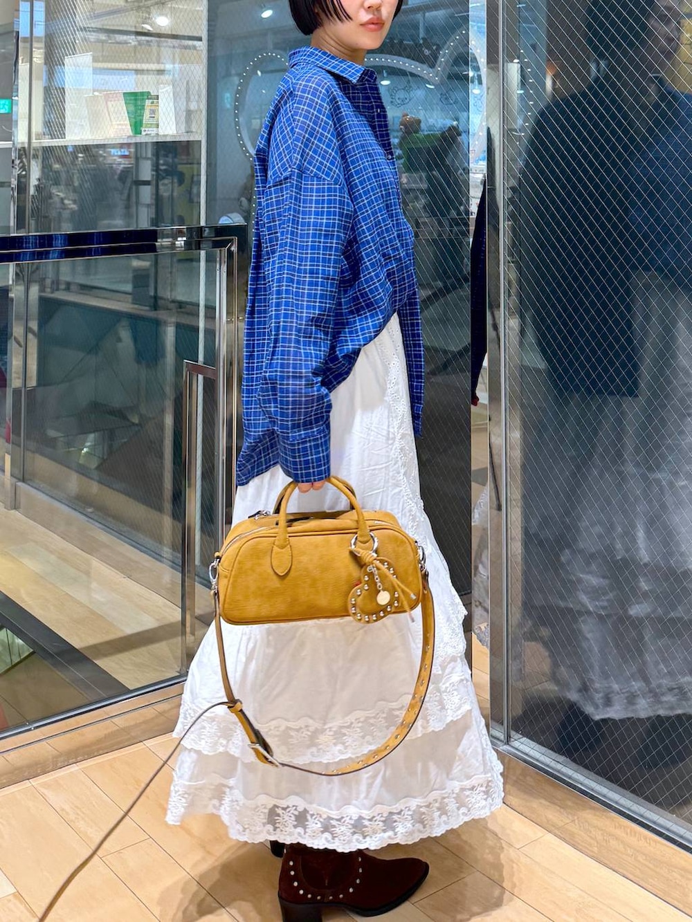 ブラウン系のボストンバッグ、ブラウン系のブーツ、ホワイト系のスカートを着用したレディースの春コーディネートの3枚目の写真