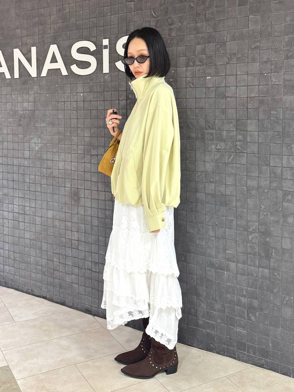 ブラウン系のボストンバッグ、ブラウン系のブーツ、ホワイト系のスカートを着用したレディースの春コーディネートの2枚目の写真