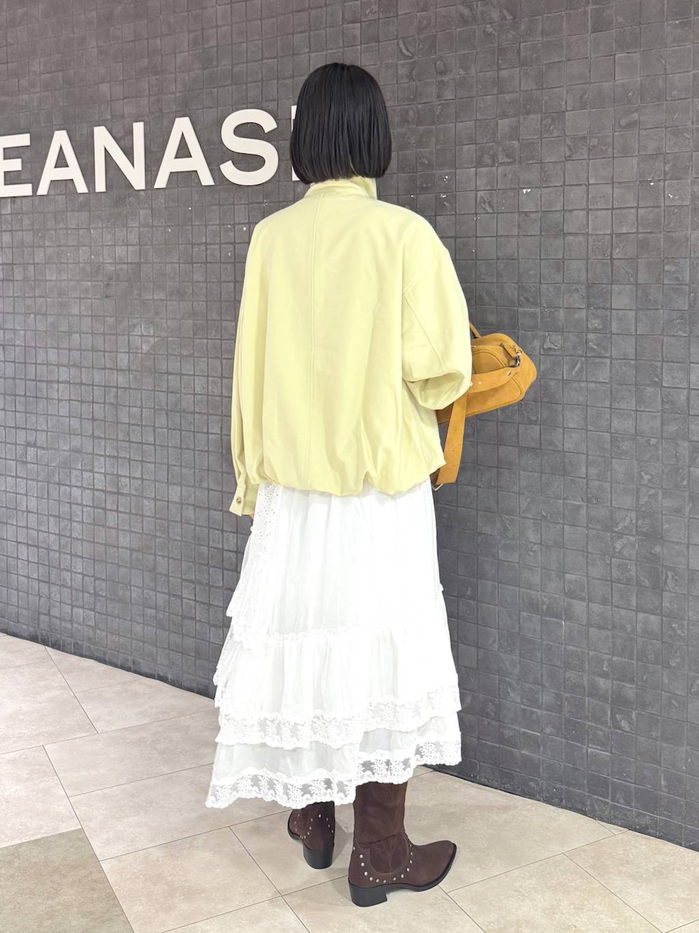 ブラウン系のボストンバッグ、ブラウン系のブーツ、ホワイト系のスカートを着用したレディースの春コーディネートの4枚目の写真