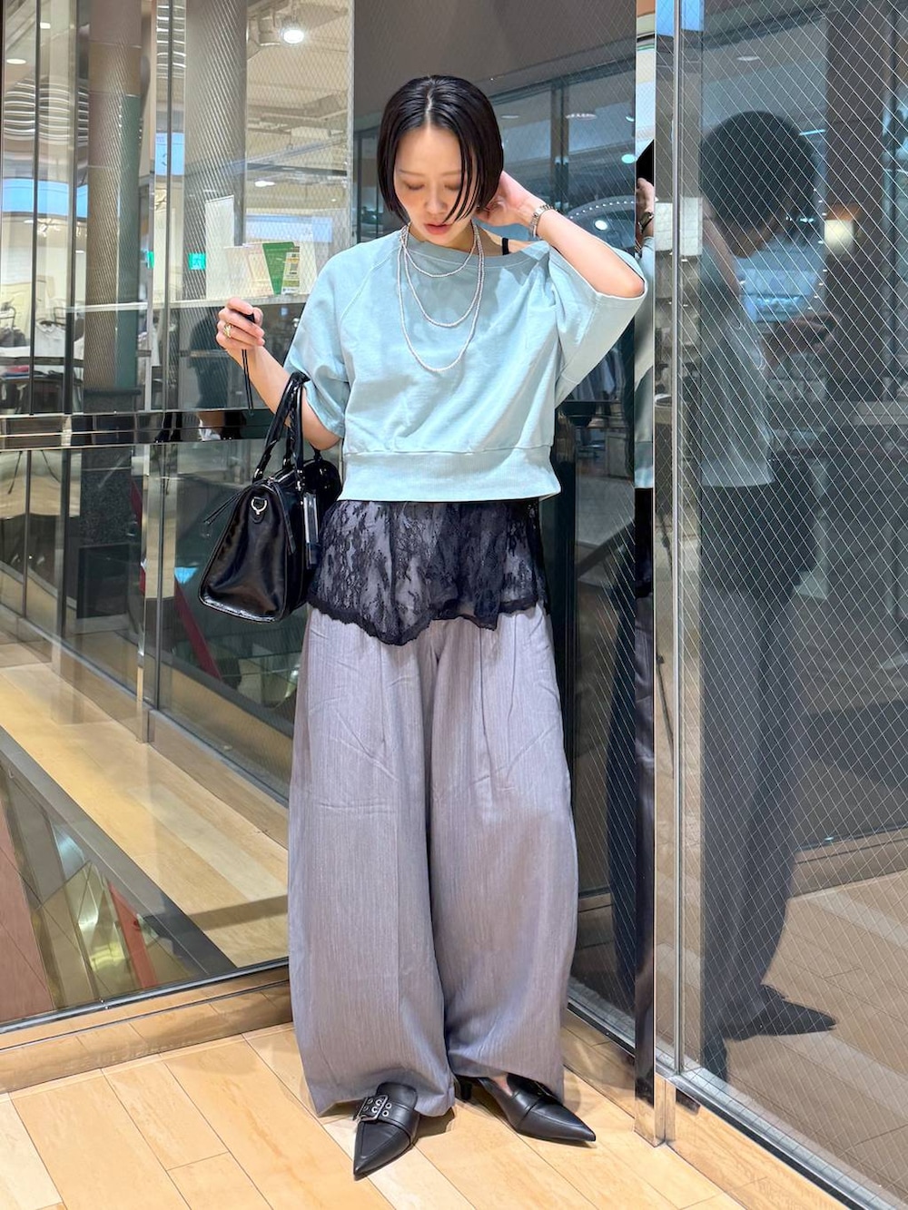 ブラック系のパンプス、ブラック系のボストンバッグ、グレー系のスラックスを着用したレディースの春コーディネートの2枚目の写真