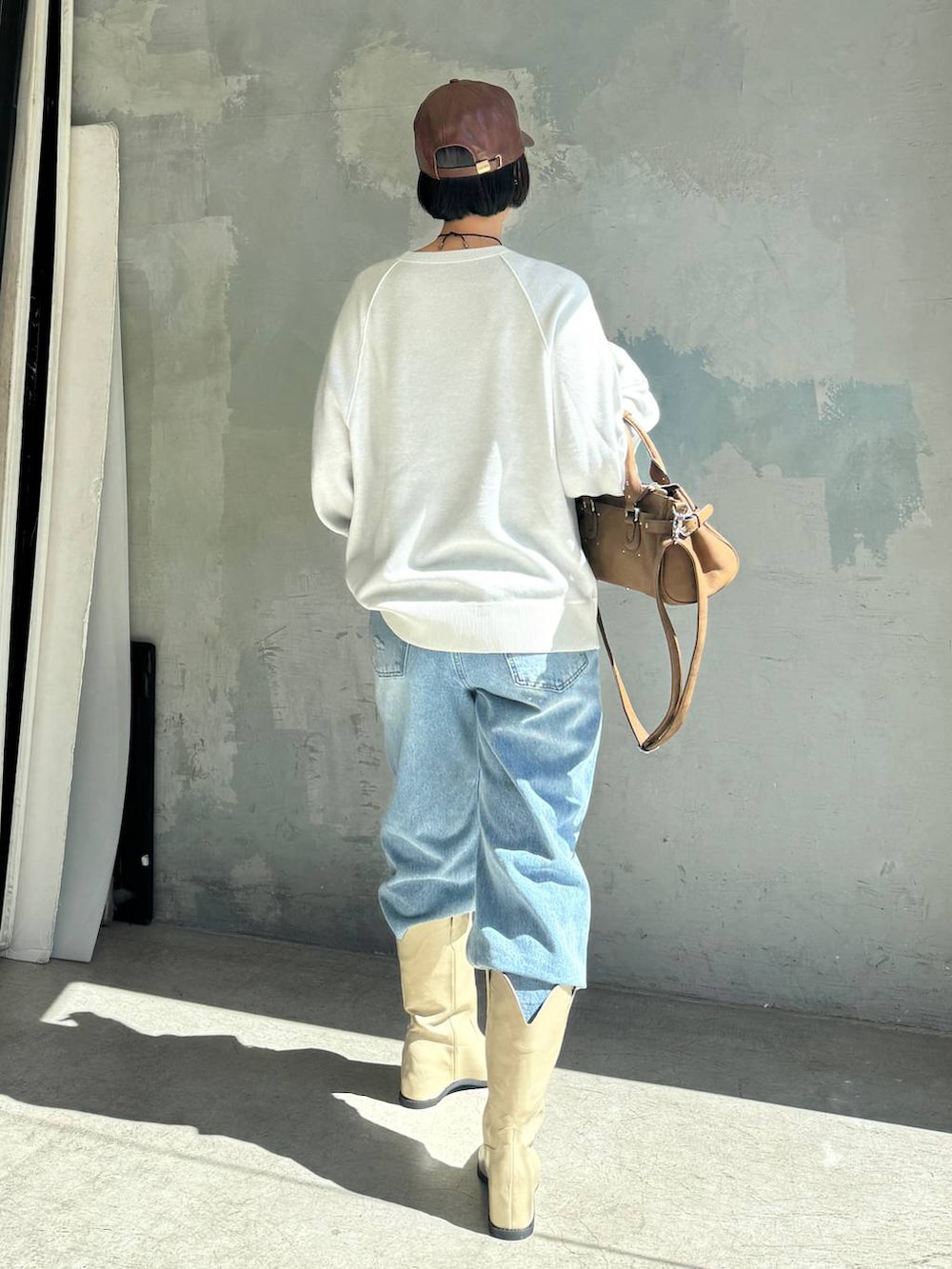 ブルー系のデニムパンツ、ホワイト系のブーツ、ブラウン系のボストンバッグを着用したレディースの秋コーディネートの4枚目の写真