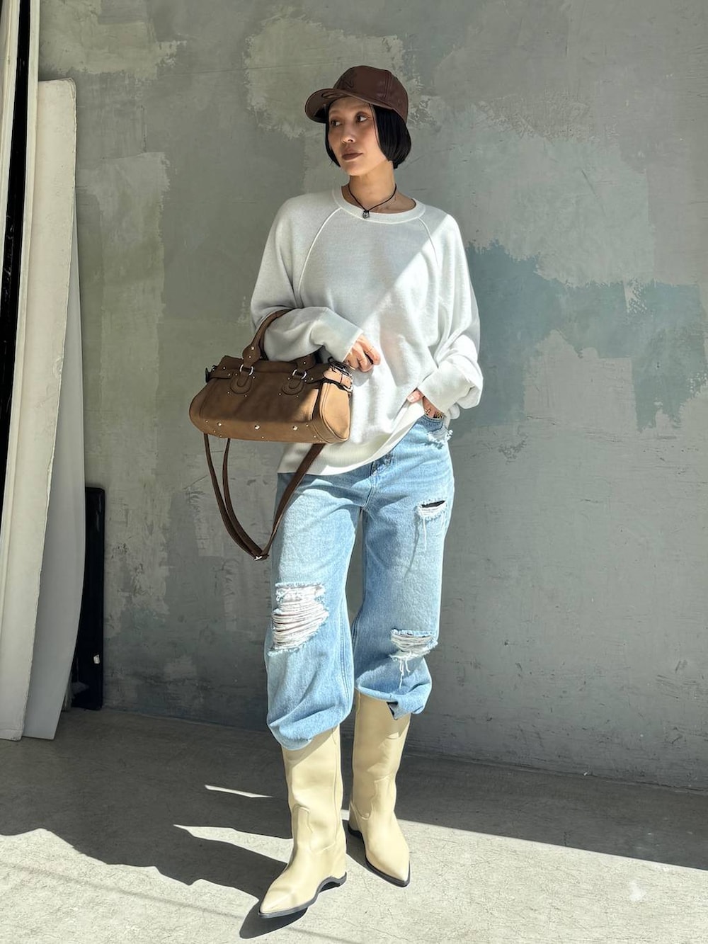 ブルー系のデニムパンツ、ホワイト系のブーツ、ブラウン系のボストンバッグを着用したレディースの秋コーディネートの5枚目の写真