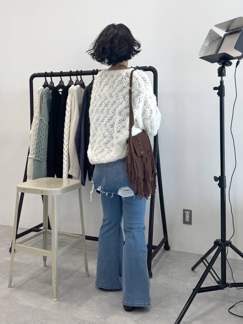 ブラウン系のショルダーバッグ、ブルー系のデニムスカート、ホワイト系のニット/セーターを着用したレディースの秋コーディネートの2枚目の写真