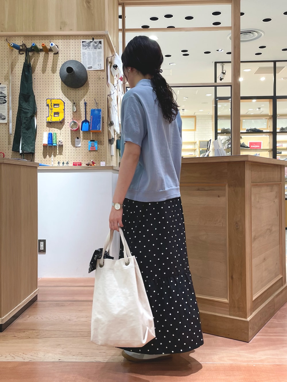 ブラック系のスカート、ブルー系のポロシャツ、ホワイト系のトートバッグを着用したレディースの春コーディネートの3枚目の写真