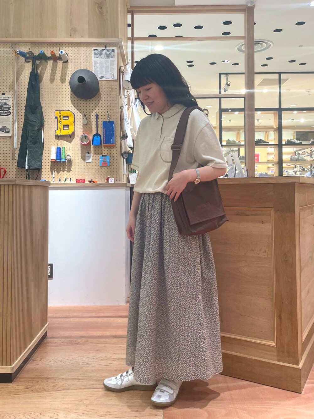 イエロー系のスカート、ブラウン系のショルダーバッグ、ホワイト系のポロシャツを着用したレディースの春コーディネートの2枚目の写真