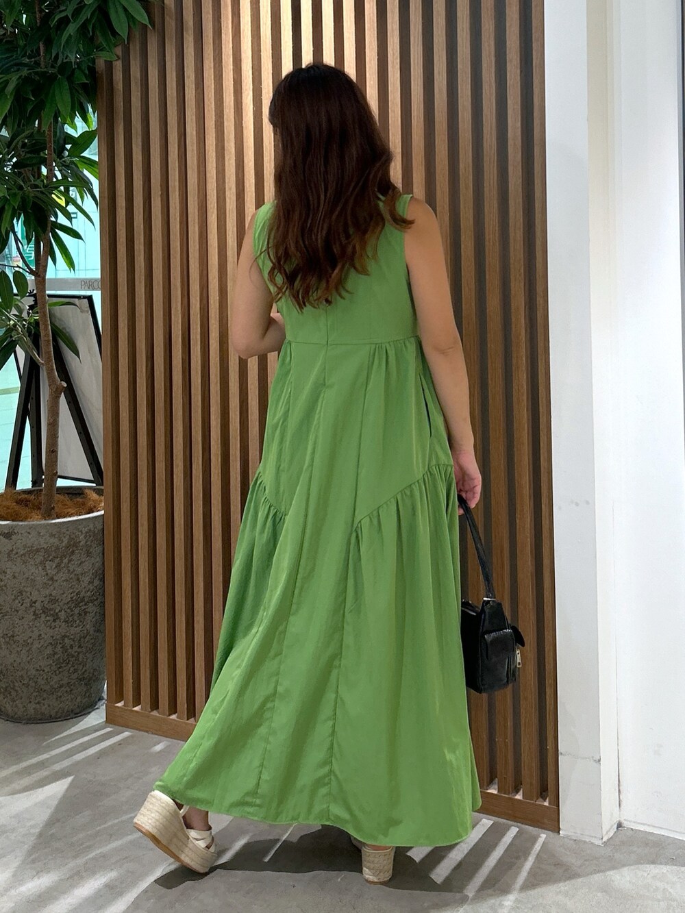 グリーン系のワンピース、ブラック系のハンドバッグ、ホワイト系のサンダルを着用したレディースの夏コーディネートの2枚目の写真