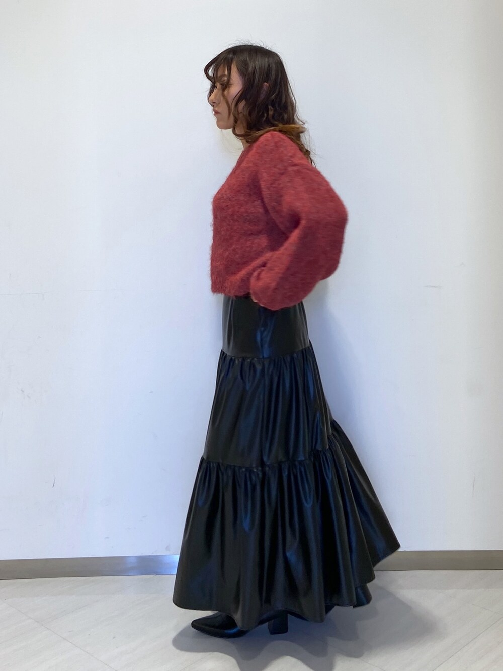 レッド系のニット/セーター、ブラック系のスカート、ブラック系のブーツを着用したレディースの秋コーディネートの3枚目の写真