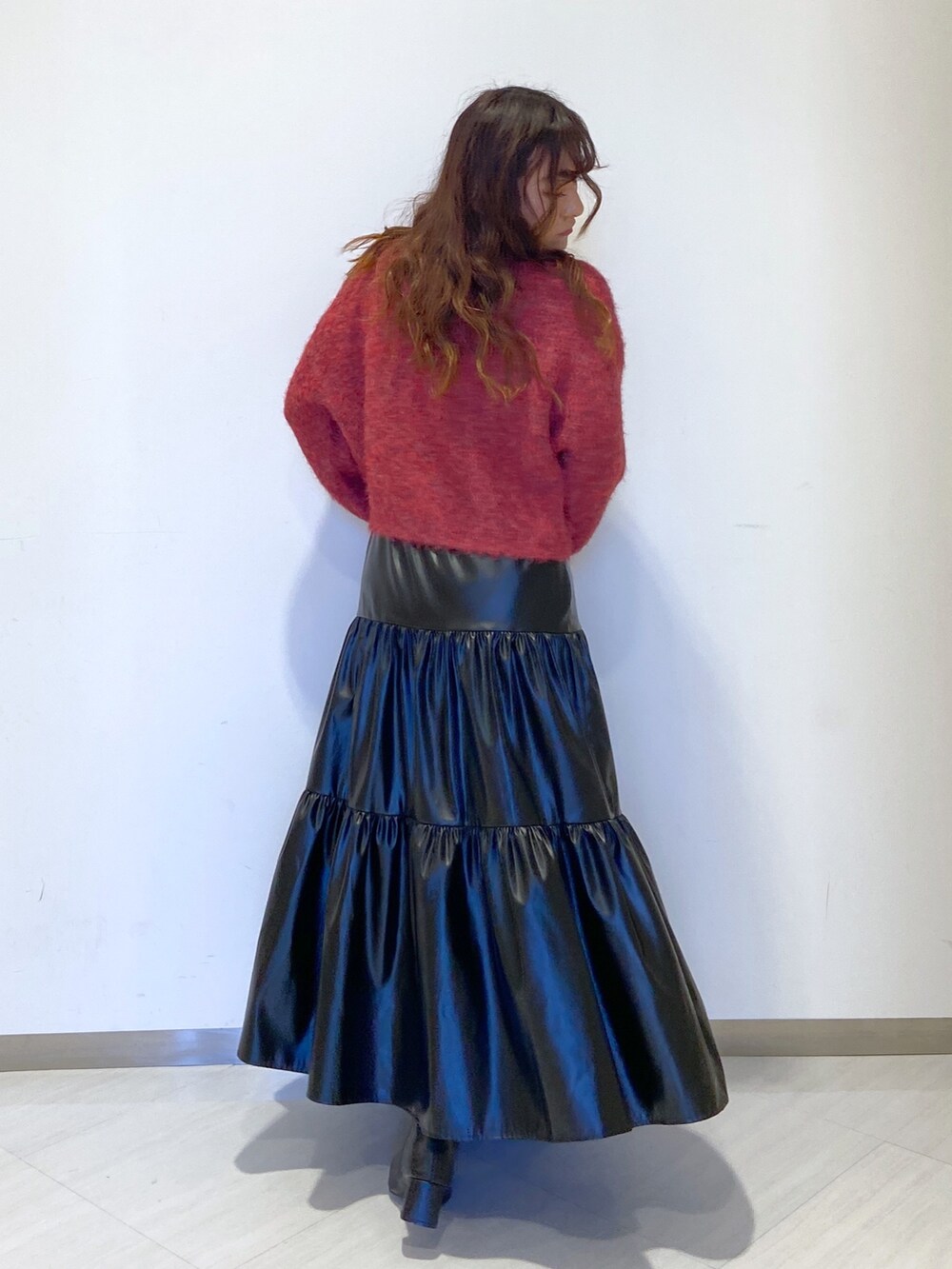 レッド系のニット/セーター、ブラック系のスカート、ブラック系のブーツを着用したレディースの秋コーディネートの2枚目の写真