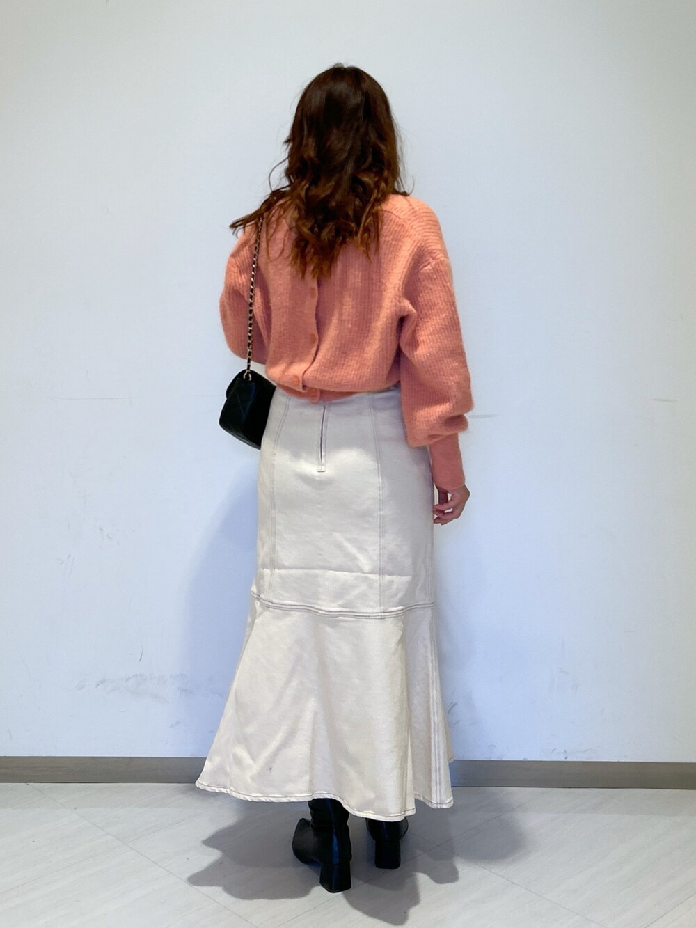 ピンク系のニット/セーター、ブラック系のショルダーバッグ、ホワイト系のデニムスカートを着用したレディースの冬コーディネートの3枚目の写真