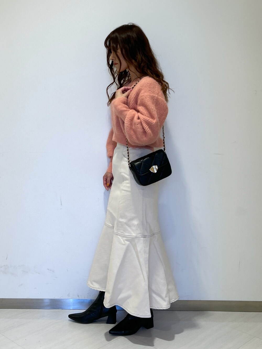 ピンク系のニット/セーター、ブラック系のショルダーバッグ、ホワイト系のデニムスカートを着用したレディースの冬コーディネートの2枚目の写真