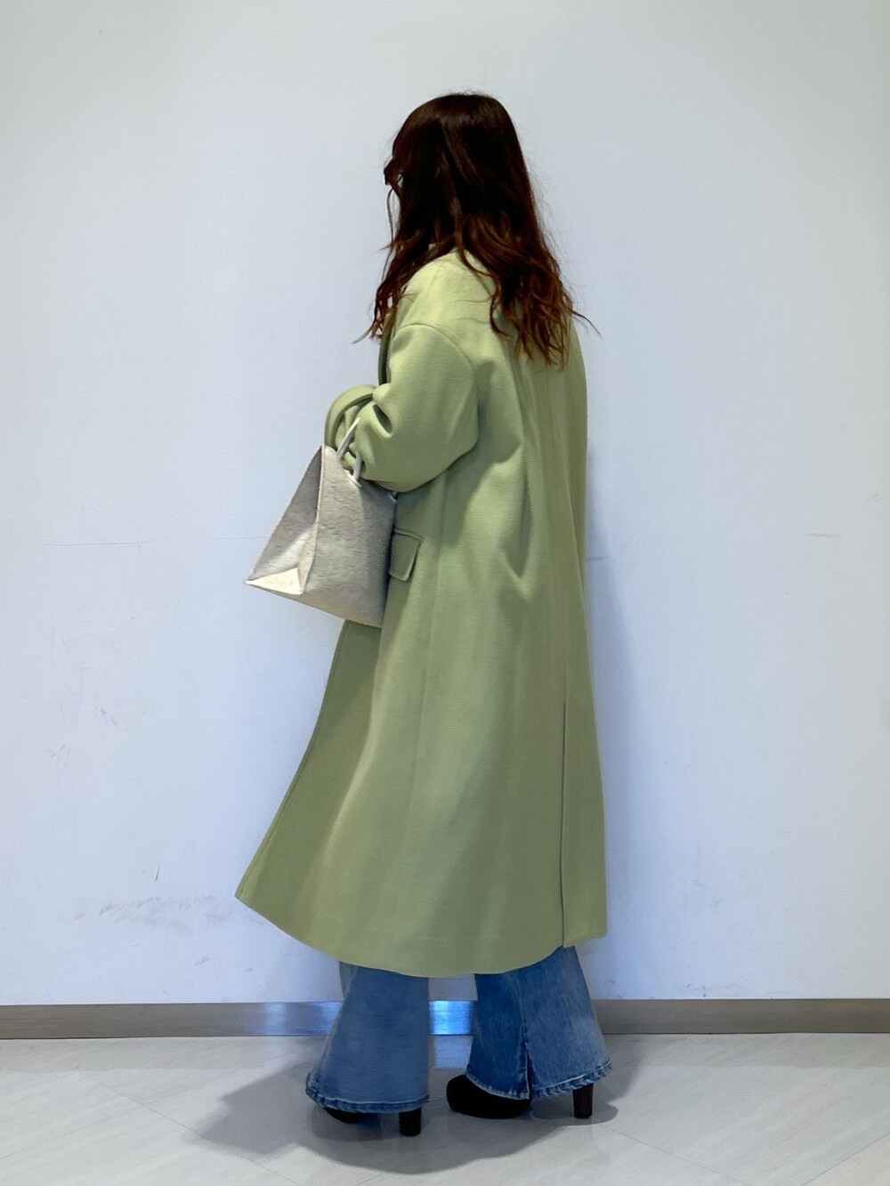 グリーン系のチェスターコート、ホワイト系のトートバッグ、ブルー系のデニムパンツを着用したレディースの冬コーディネートの2枚目の写真