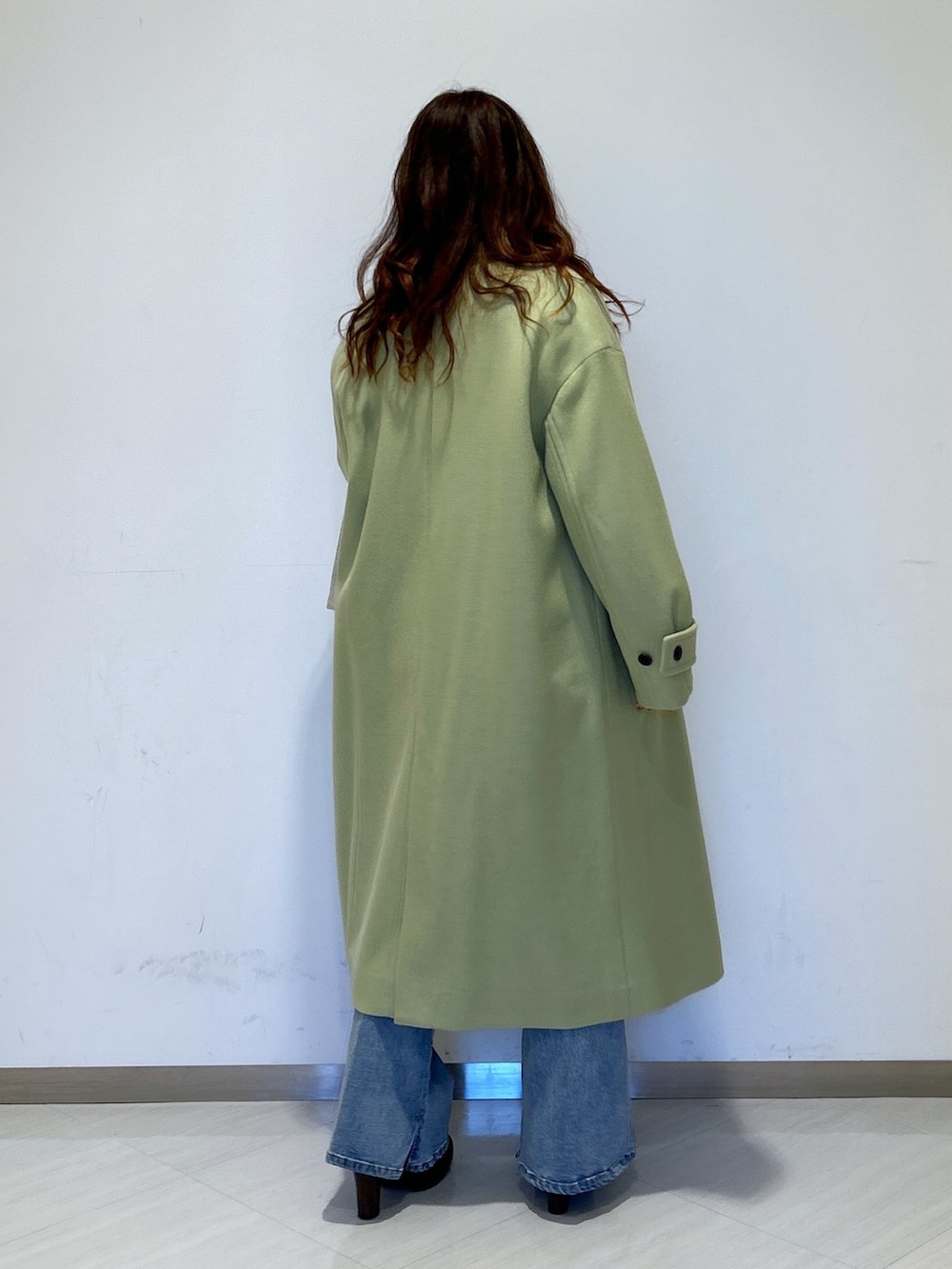 グリーン系のチェスターコート、ホワイト系のトートバッグ、ブルー系のデニムパンツを着用したレディースの冬コーディネートの3枚目の写真