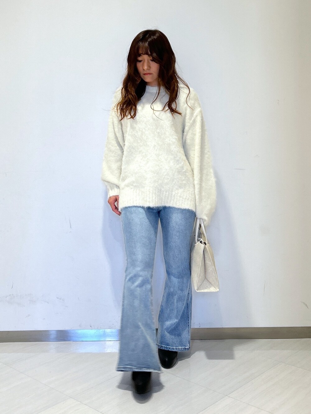 グリーン系のチェスターコート、ホワイト系のトートバッグ、ブルー系のデニムパンツを着用したレディースの冬コーディネートの5枚目の写真