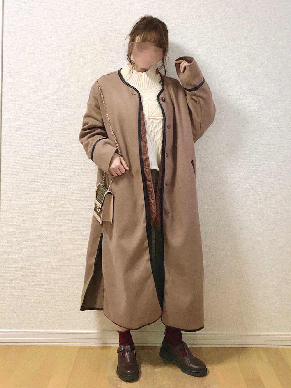ブラウン系のノーカラーコート、ベージュ系のベスト、ブラウン系のスカートを着用したレディースの冬コーディネートの2枚目の写真