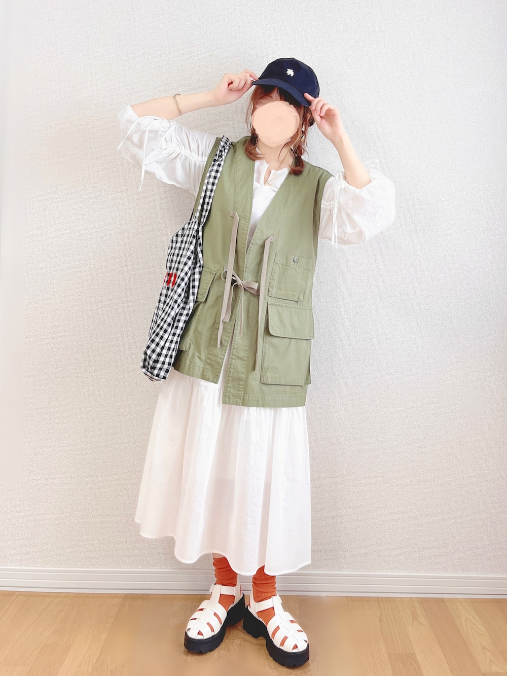 グリーン系のベスト、ホワイト系のワンピース、ブラック系のトートバッグを着用したレディースの夏コーディネートの2枚目の写真