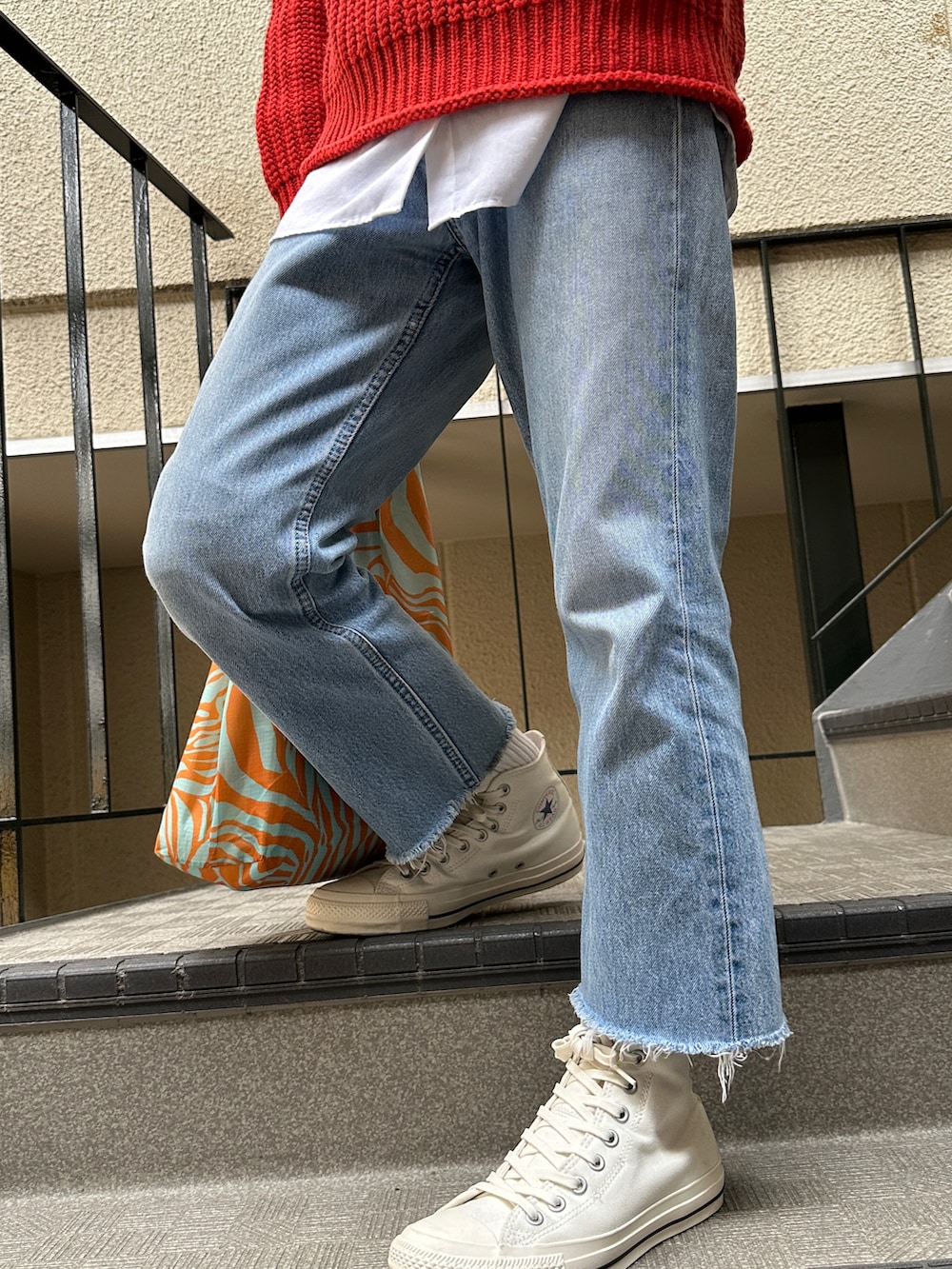 オレンジ系のニット/セーター、ブルー系のデニムパンツ、ホワイト系のスニーカーを着用したメンズの秋コーディネートの3枚目の写真