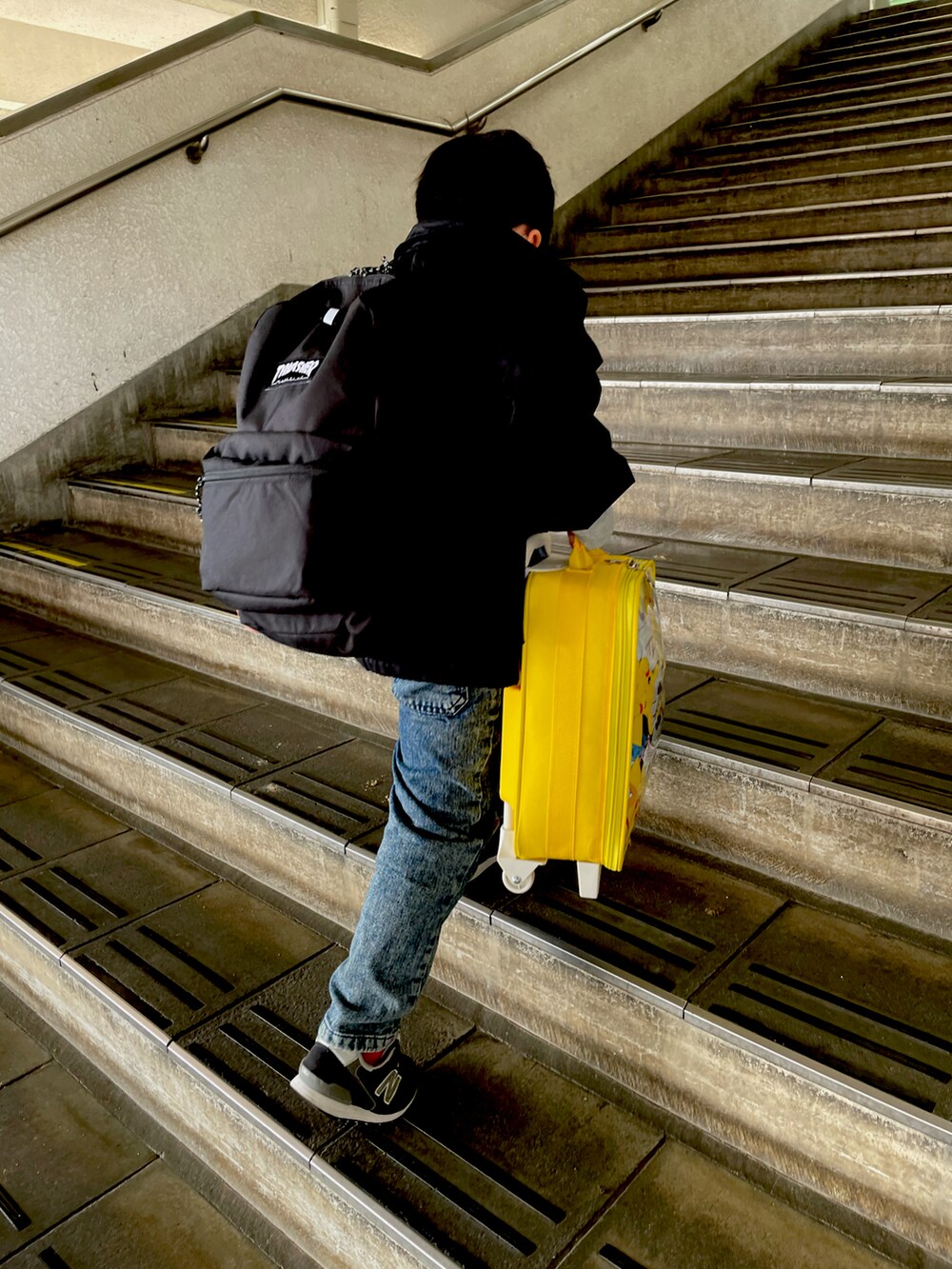 イエロー系のスーツケース/キャリーバッグ、ブラック系のその他アウター、グレー系のスウェットを着用したキッズの春コーディネートの2枚目の写真