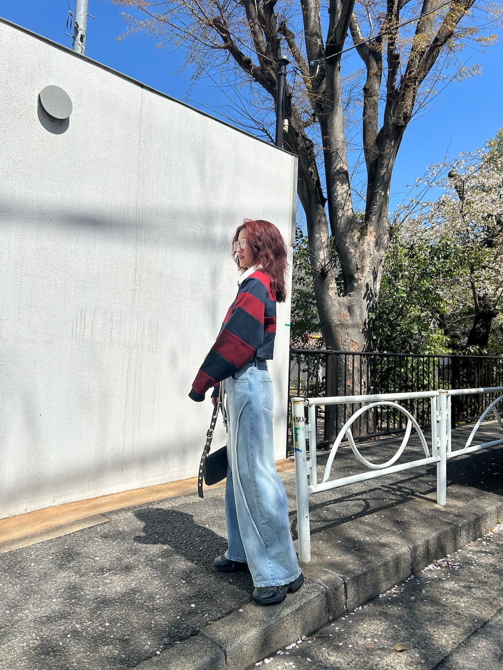 レッド系のポロシャツ、ブルー系のデニムパンツ、ブラック系のスニーカーを着用したレディースの春コーディネートの3枚目の写真