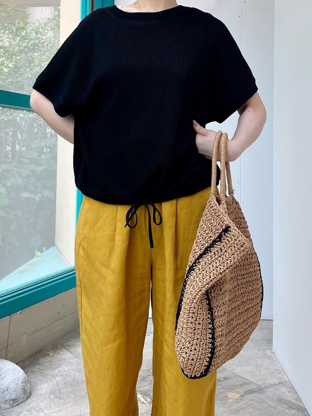 ブラック系のニット/セーター、イエロー系のその他パンツ、ベージュ系のトートバッグを着用したレディースの夏コーディネートの4枚目の写真