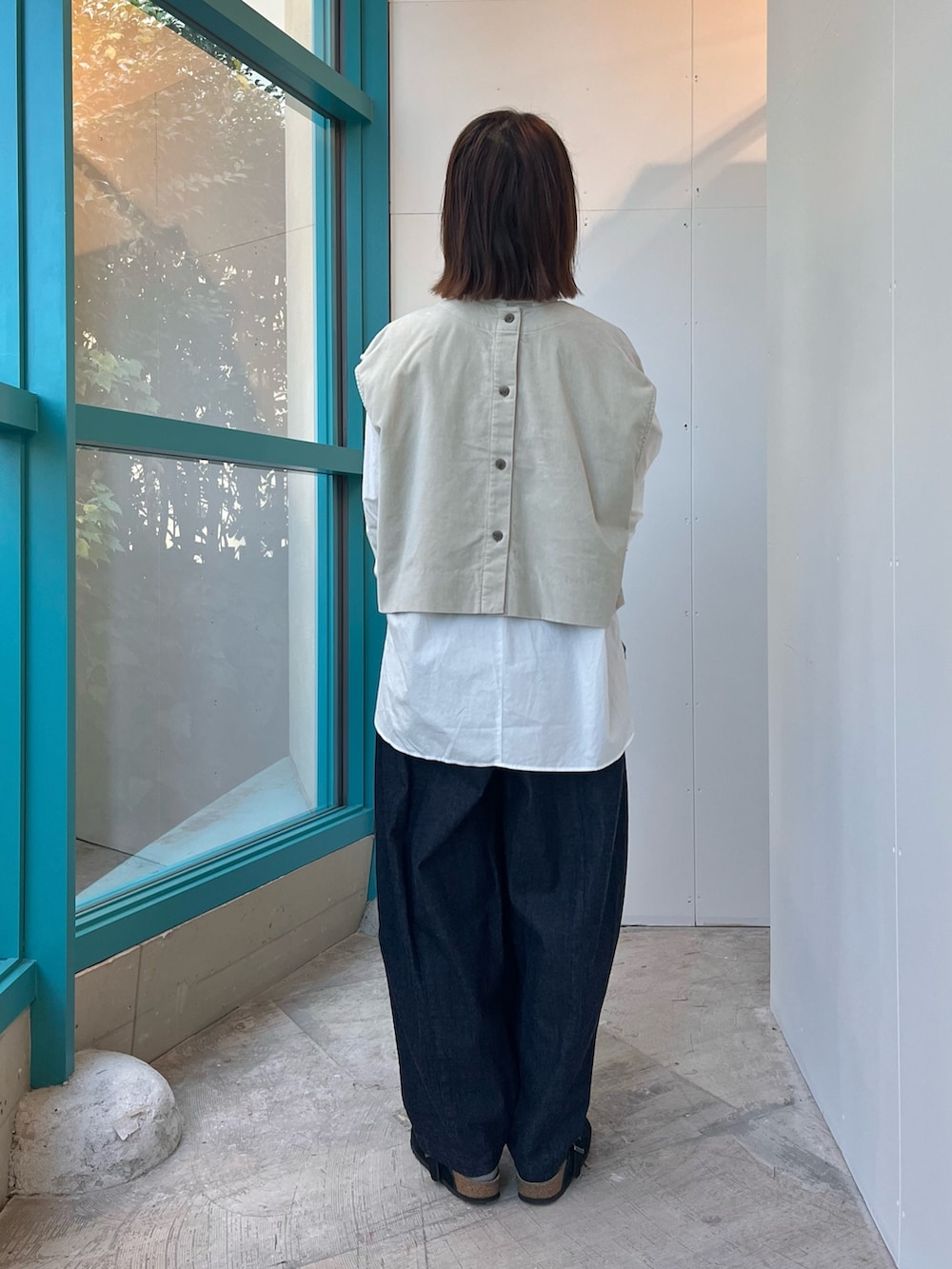 グレー系のベスト、ホワイト系のシャツ/ブラウス、ブラック系のサンダルを着用したレディースの秋コーディネートの3枚目の写真