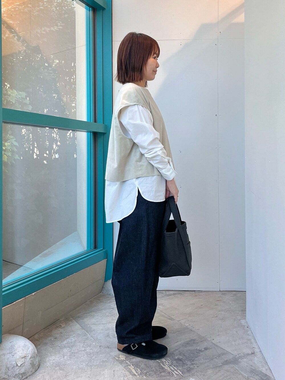 グレー系のベスト、ホワイト系のシャツ/ブラウス、ブラック系のサンダルを着用したレディースの秋コーディネートの2枚目の写真