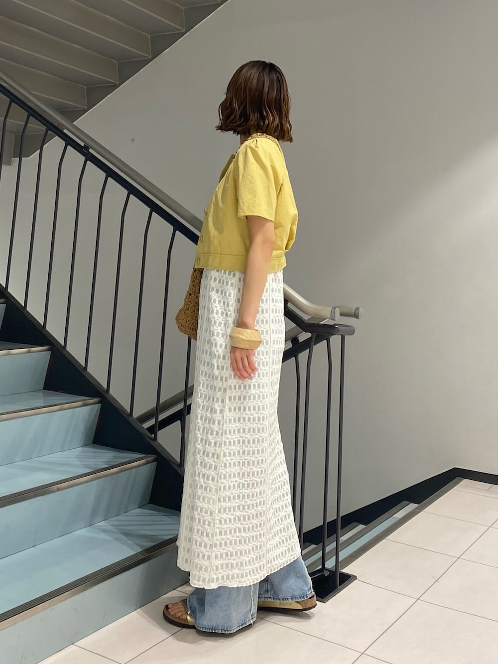 ホワイト系のワンピース、ブルー系のデニムパンツ、イエロー系のトートバッグを着用したレディースの夏コーディネートの2枚目の写真