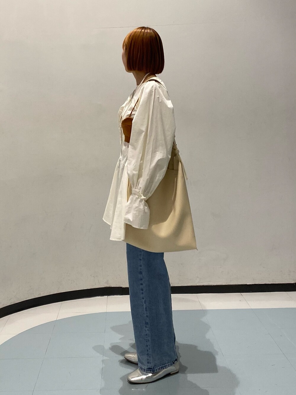 ブラウン系のベスト、ホワイト系のトートバッグ、ブルー系のデニムパンツを着用したレディースの春コーディネートの2枚目の写真