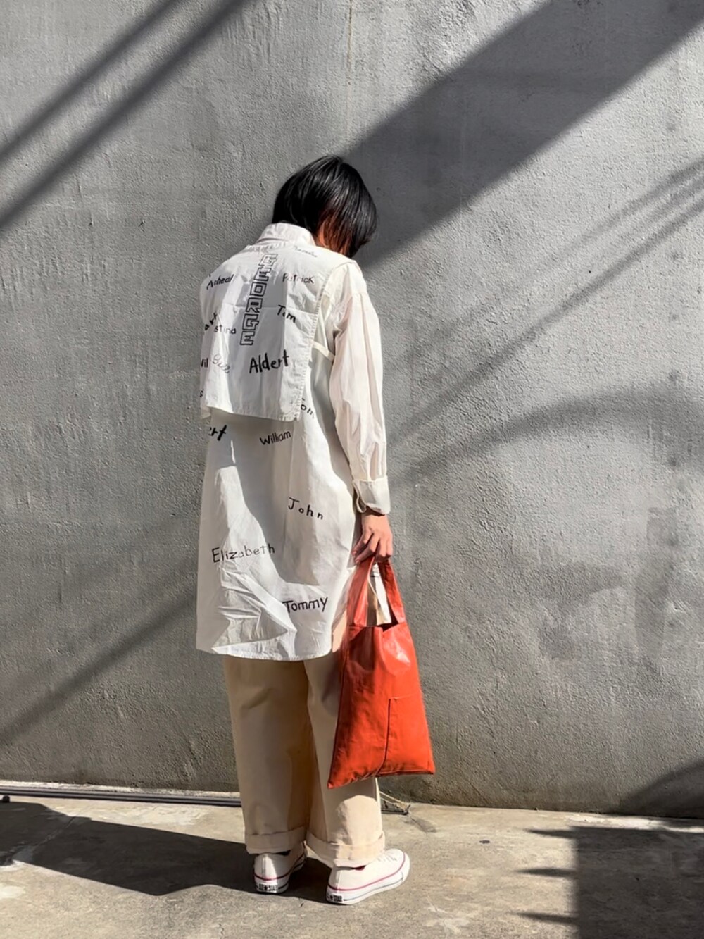 オレンジ系のトートバッグ、ホワイト系のベスト、ホワイト系のワンピースを着用したレディースの秋コーディネートの2枚目の写真