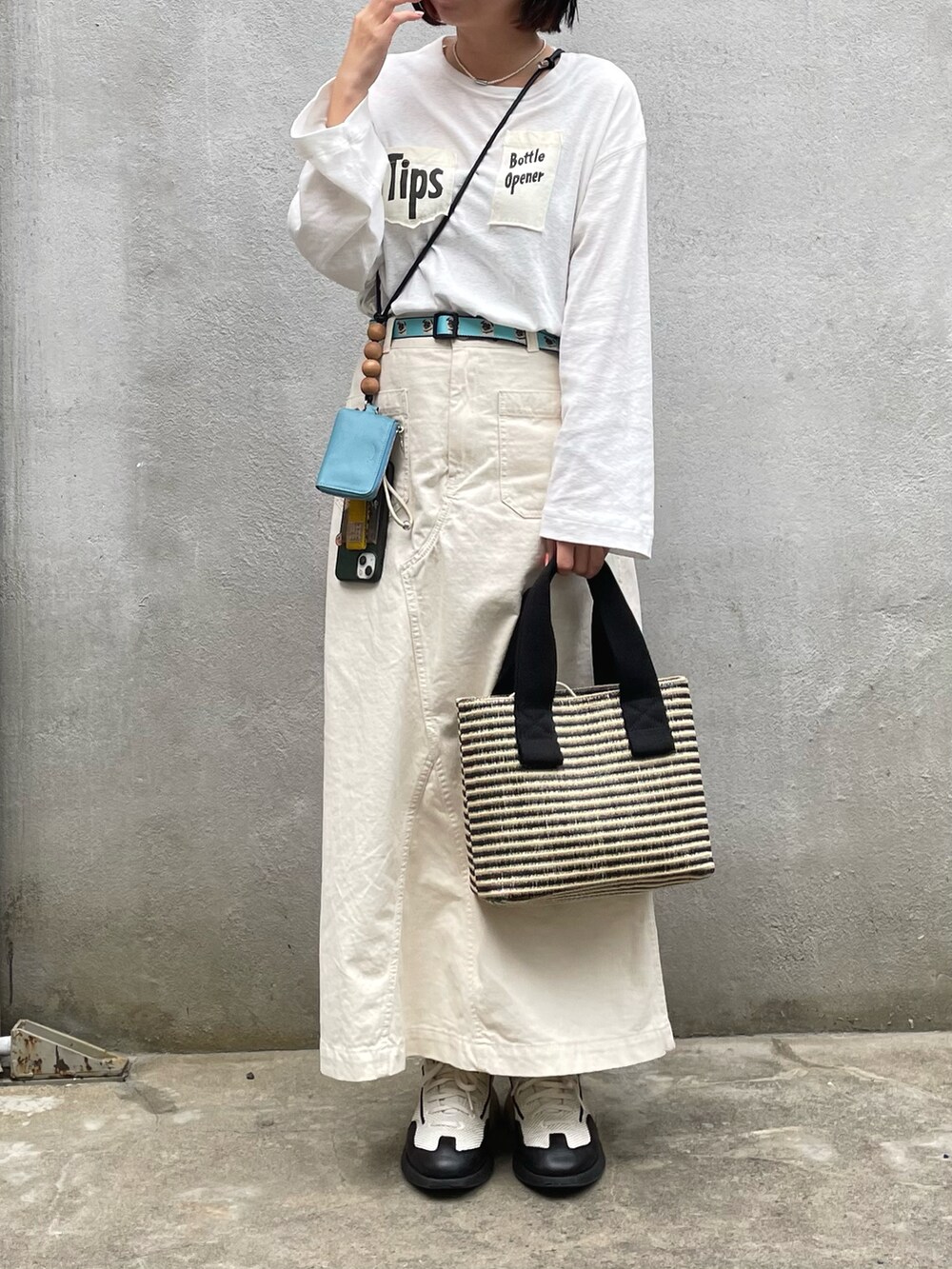 ホワイト系のスニーカー、ベージュ系のスカート、ブラック系のトートバッグを着用したレディースの春コーディネートの2枚目の写真