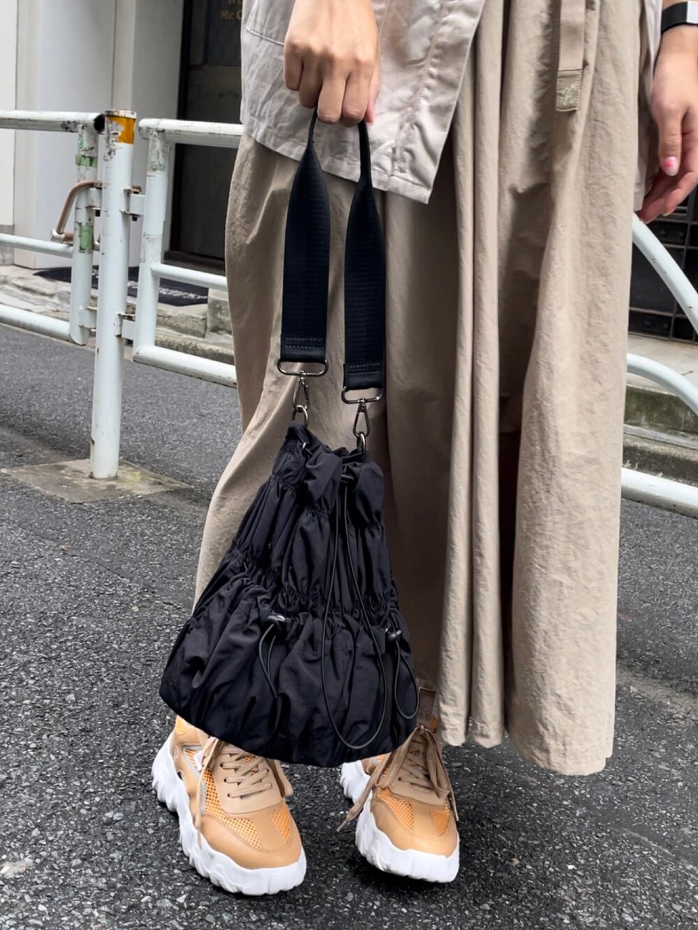 ブラック系のトートバッグ、ベージュ系のスカート、ベージュ系のスニーカーを着用したレディースの夏コーディネートの2枚目の写真