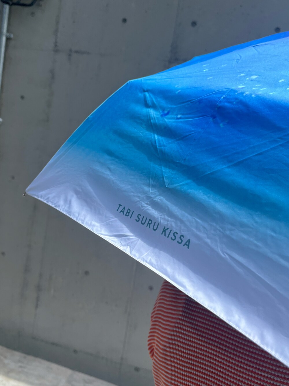 ブルー系のトートバッグ、ホワイト系のスニーカー、ブルー系の折りたたみ傘を着用したレディースの夏コーディネートの3枚目の写真