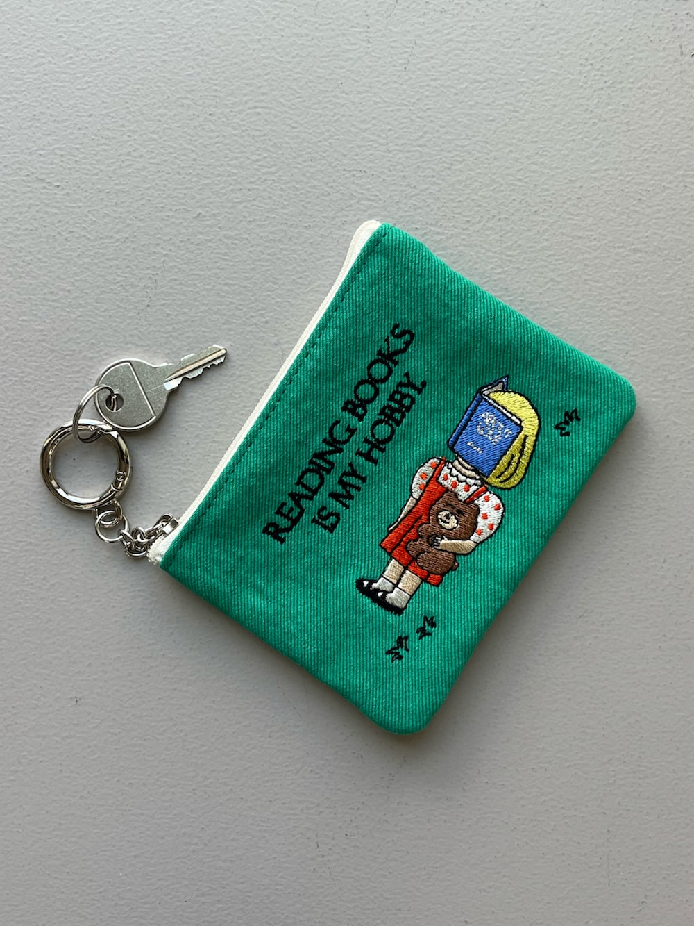 シルバー系のチャーム、ベージュ系の財布、グリーン系のポーチを着用したレディースの秋コーディネートの2枚目の写真