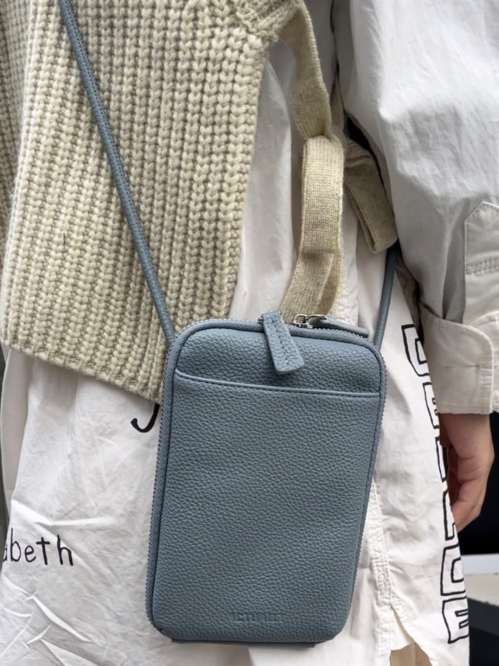 ブルー系のショルダーバッグ、ホワイト系のワンピース、ホワイト系のベストを着用したレディースの秋コーディネートの2枚目の写真