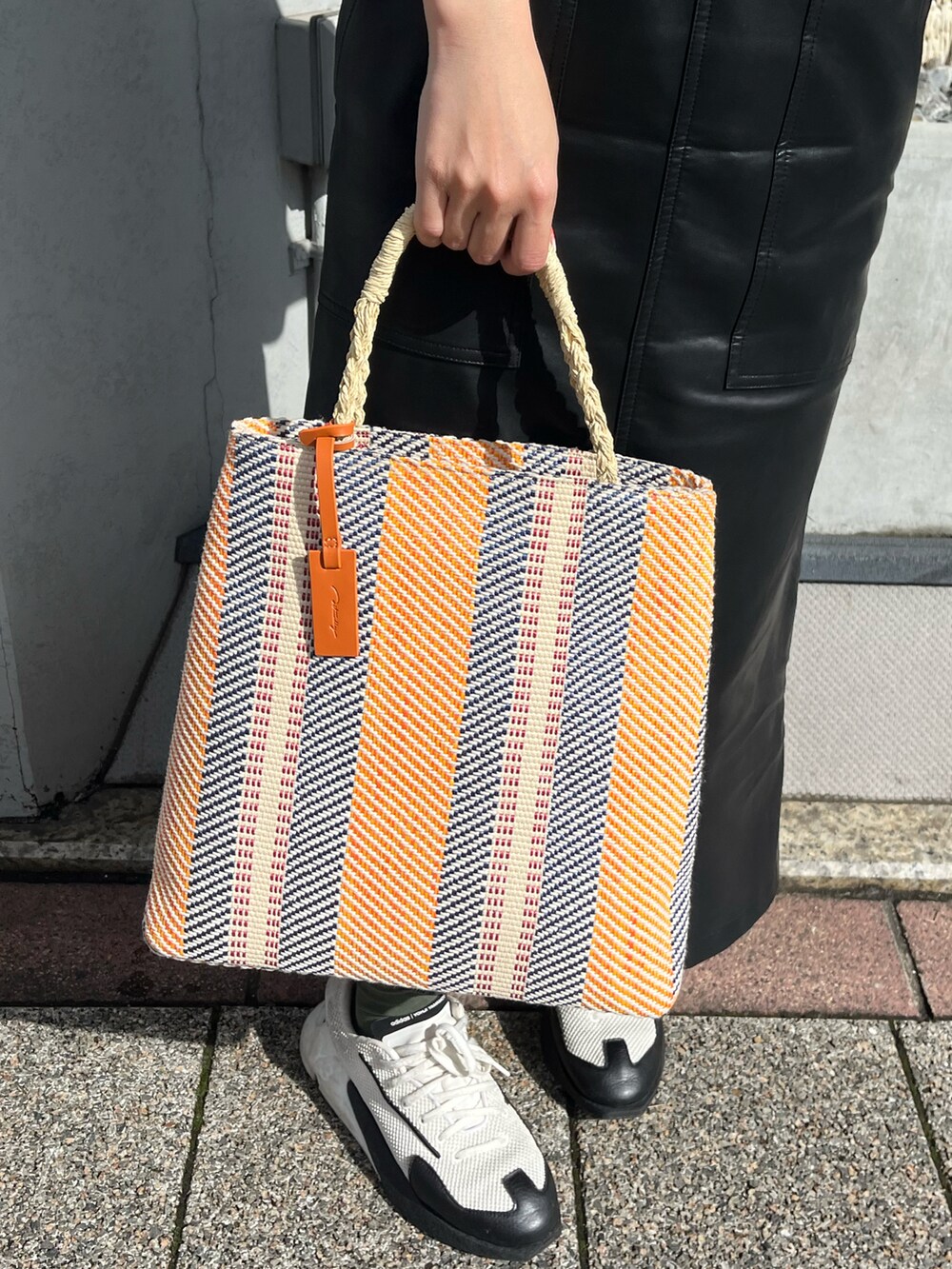 ホワイト系のスニーカー、オレンジ系のトートバッグ、ブラック系のジャンパースカートを着用したレディースの春コーディネートの3枚目の写真