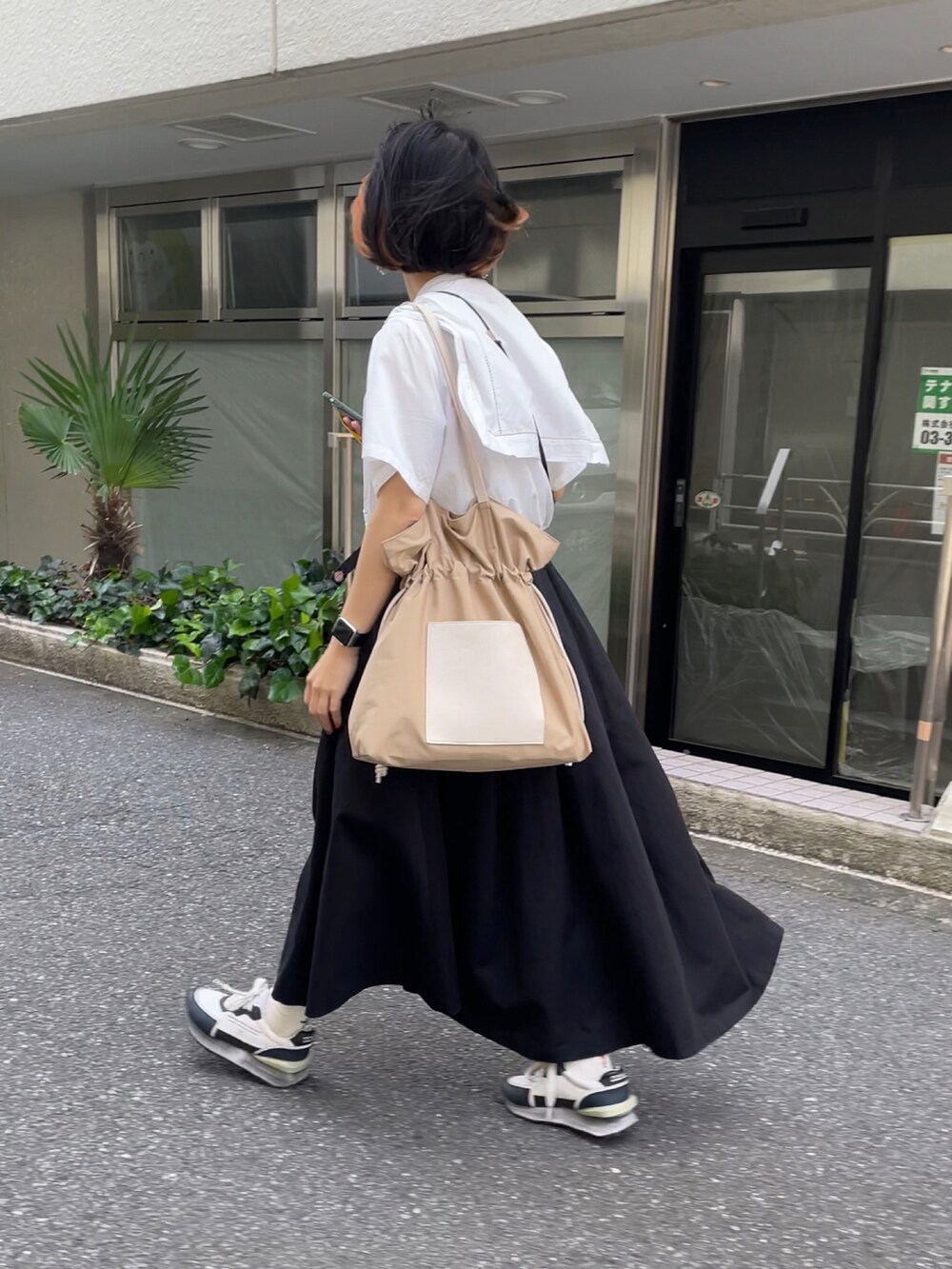 グレー系のトートバッグ、ブラック系のスカート、ホワイト系のスニーカーを着用したレディースの春コーディネートの2枚目の写真