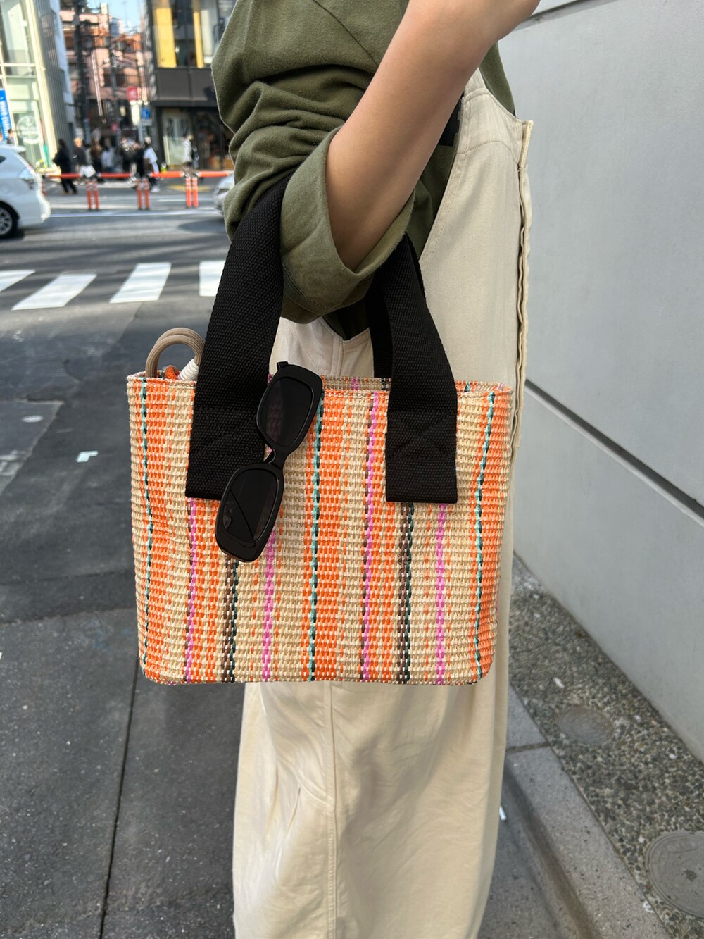 オレンジ系のトートバッグ、ホワイト系のスニーカー、ブラック系のサングラスを着用したレディースの春コーディネートの2枚目の写真