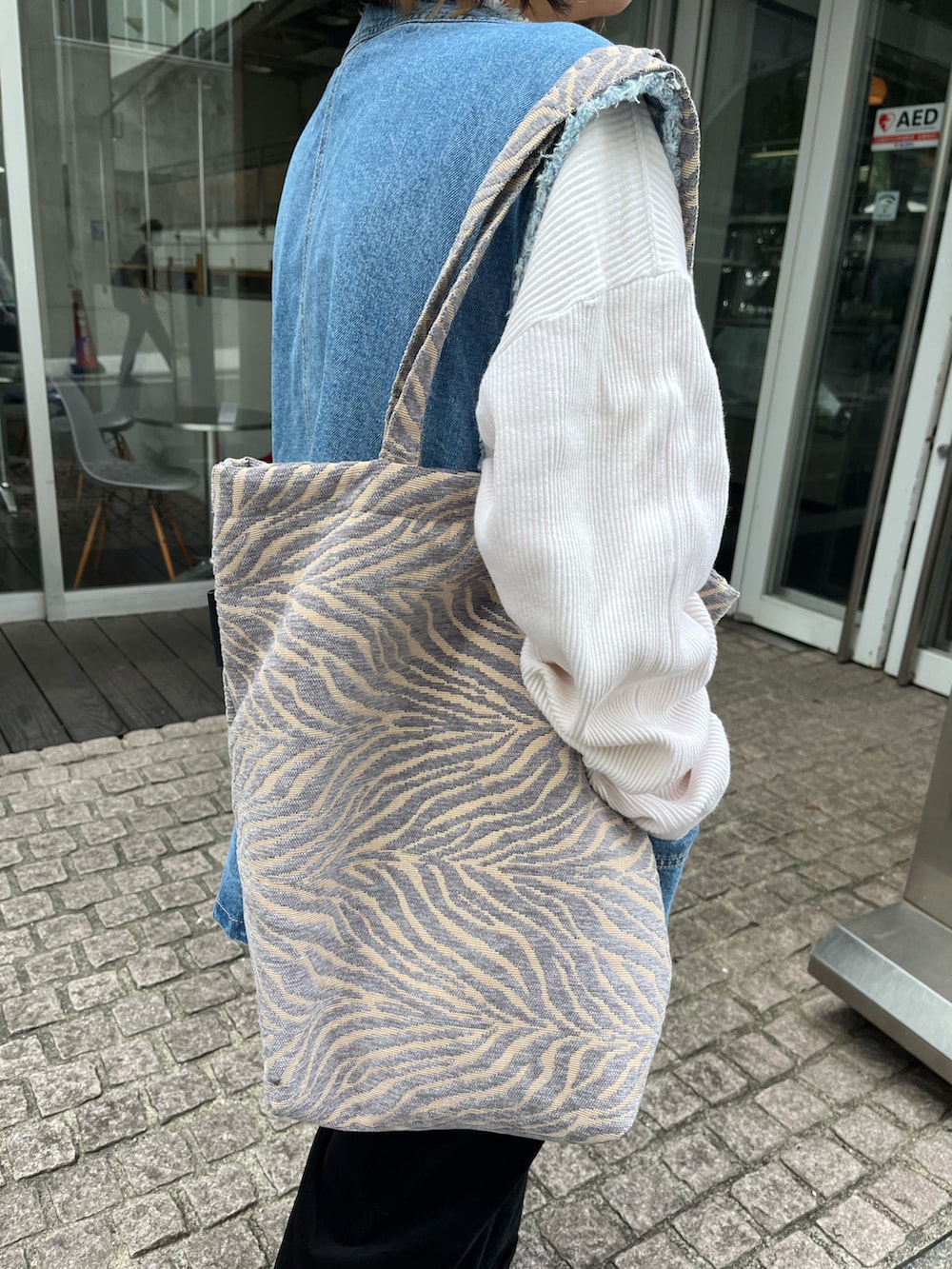 グレー系のトートバッグ、ブルー系のベスト、ホワイト系のスニーカーを着用したレディースの秋コーディネートの3枚目の写真