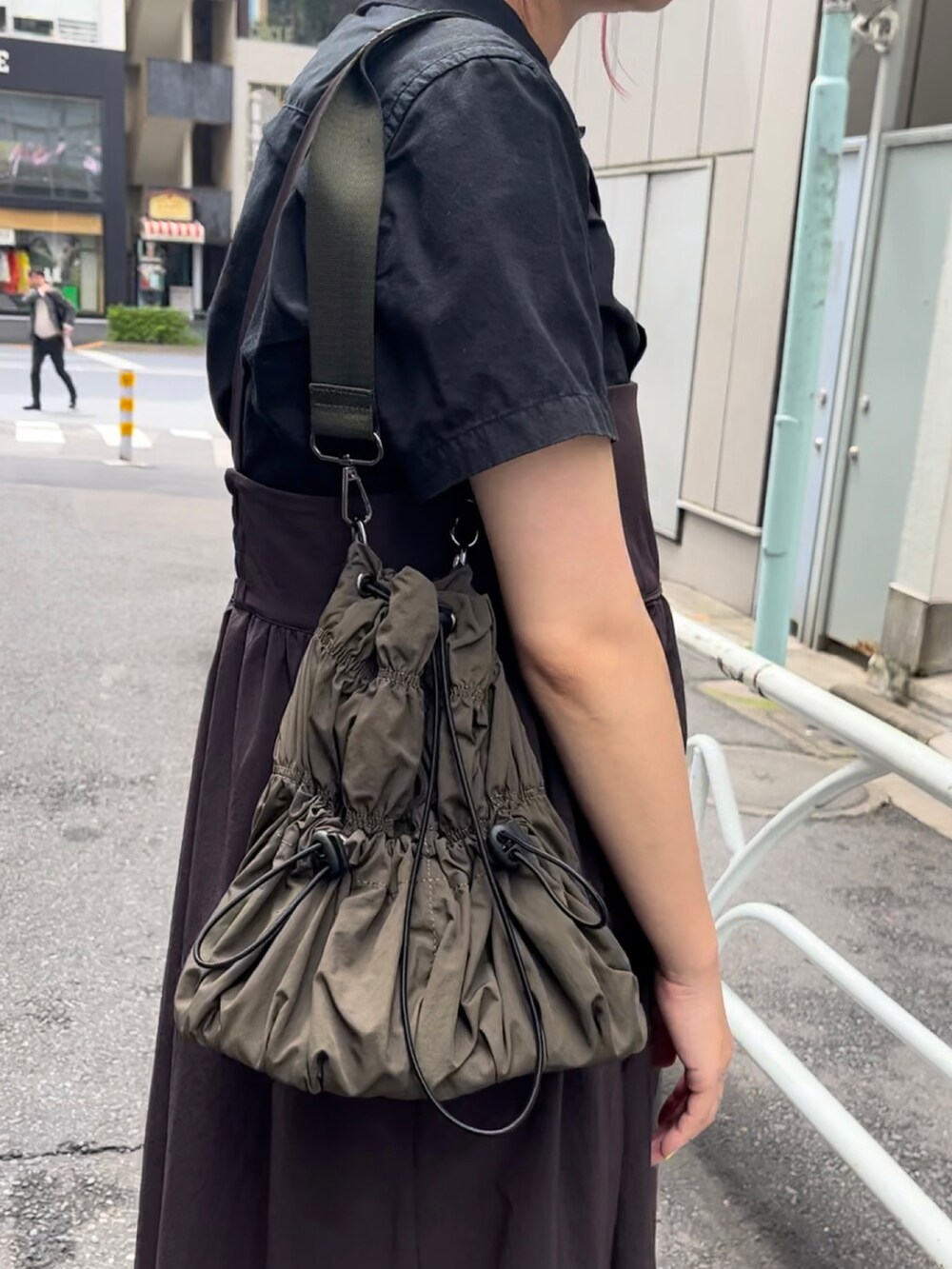 グリーン系のトートバッグ、ホワイト系のスニーカー、ブラック系のシャツ/ブラウスを着用したレディースの夏コーディネートの2枚目の写真