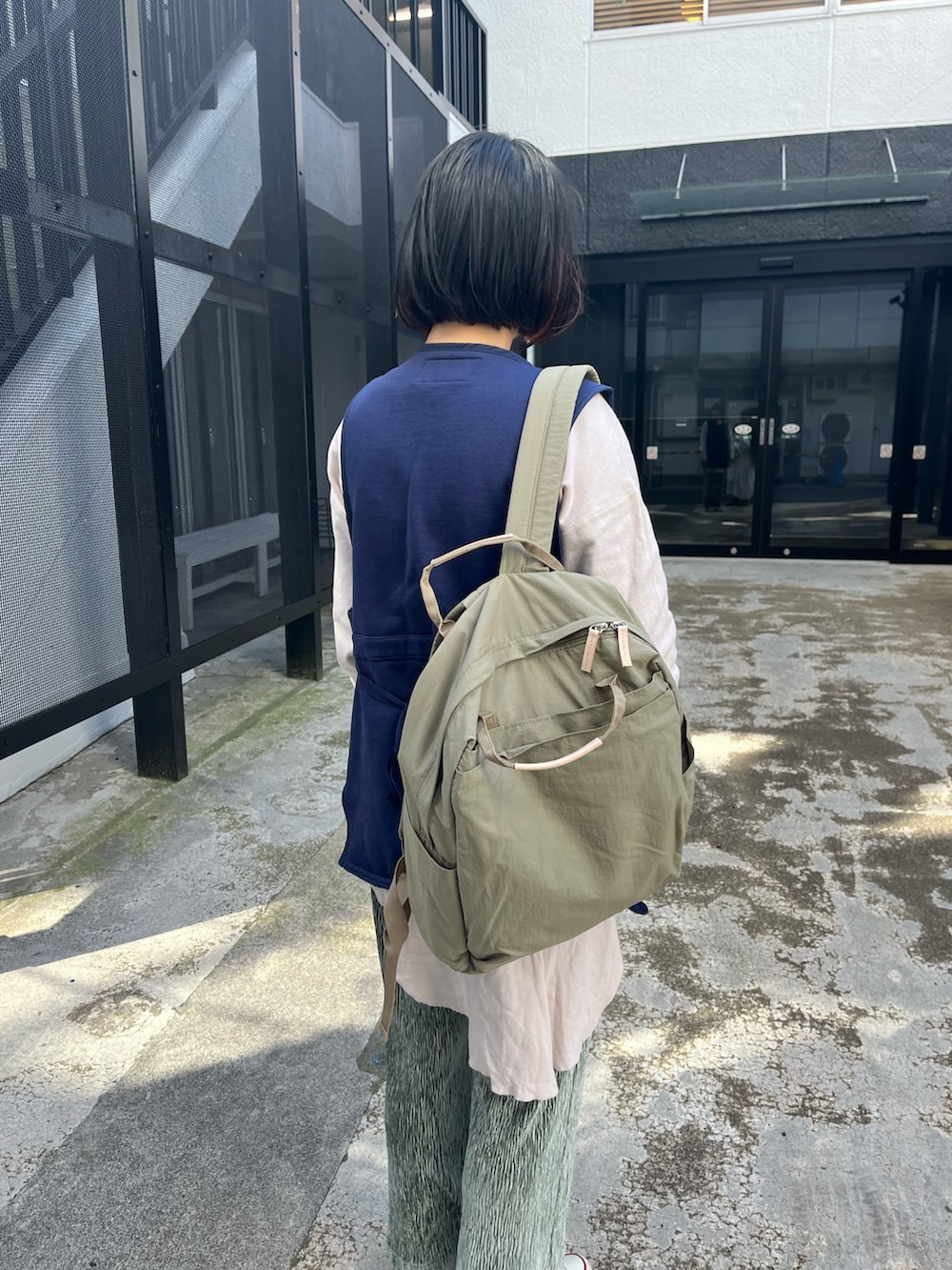 グリーン系のバックパック/リュック、ホワイト系のスニーカー、ブルー系のベストを着用したレディースの春コーディネートの2枚目の写真