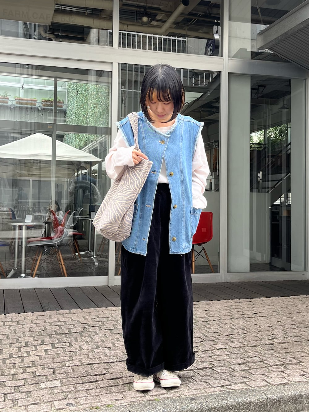 グレー系のトートバッグ、ブルー系のベスト、ホワイト系のスニーカーを着用したレディースの秋コーディネートの2枚目の写真