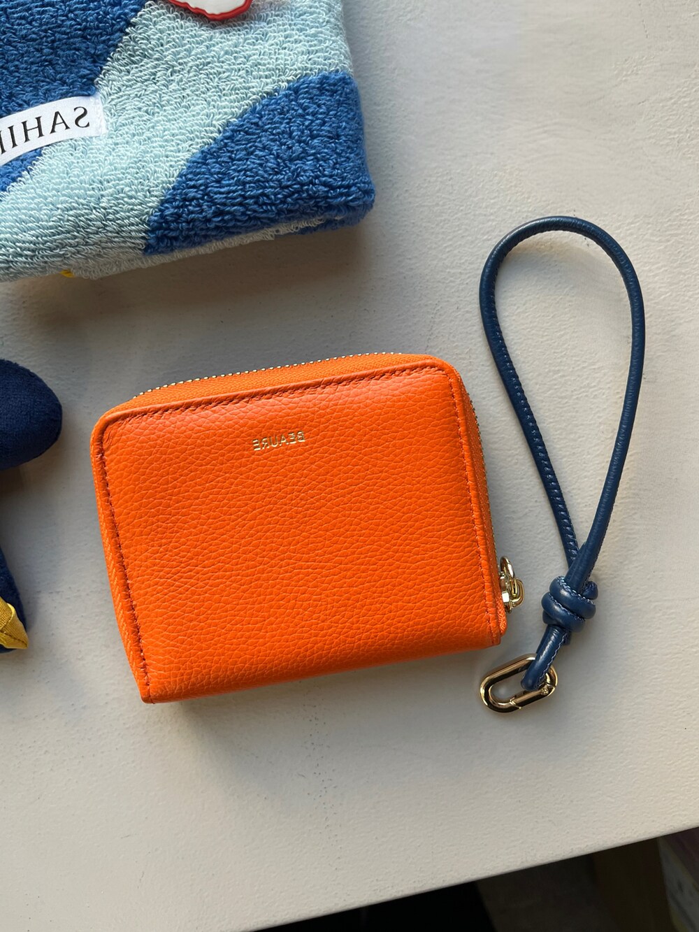 オレンジ系の財布、ブルー系のキーホルダー、ブルー系のハンカチ/ハンドタオルを着用したレディースの春コーディネートの2枚目の写真