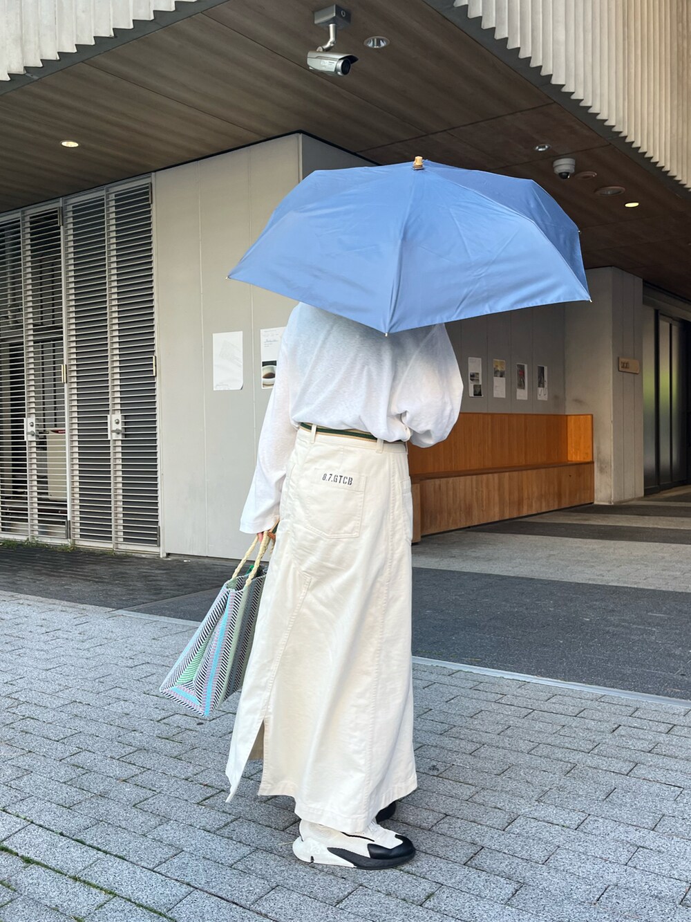 ホワイト系のスニーカー、グリーン系のトートバッグ、ベージュ系のスカートを着用したレディースの春コーディネートの2枚目の写真