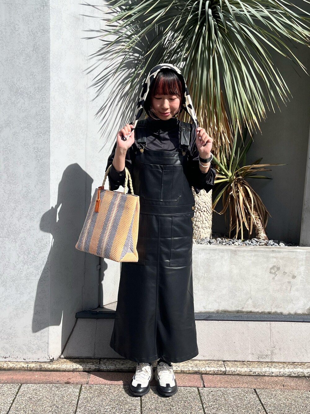 ホワイト系のスニーカー、オレンジ系のトートバッグ、ブラック系のジャンパースカートを着用したレディースの春コーディネートの2枚目の写真