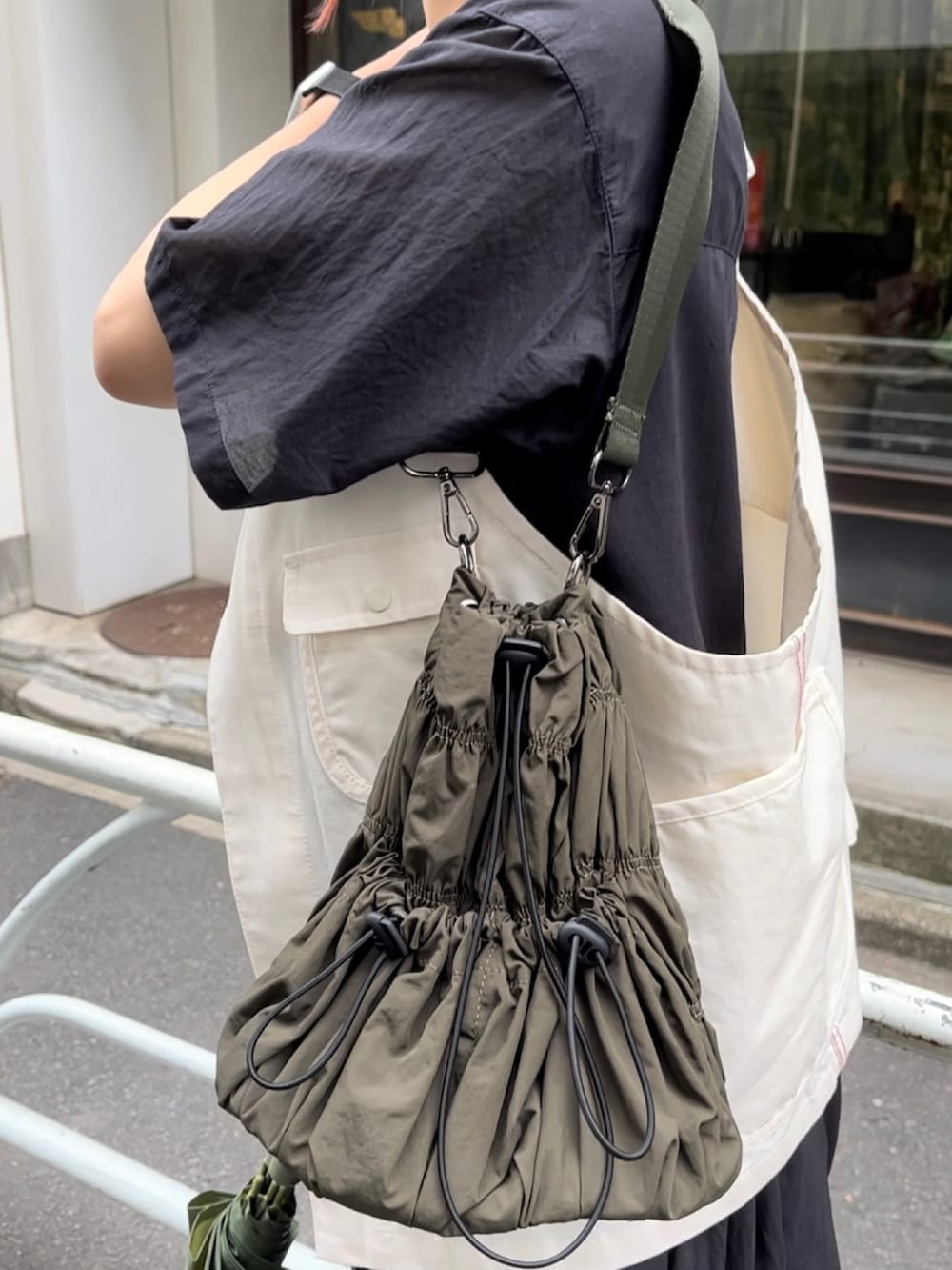 グリーン系のトートバッグ、ホワイト系のスニーカー、ホワイト系のベストを着用したレディースの夏コーディネートの3枚目の写真
