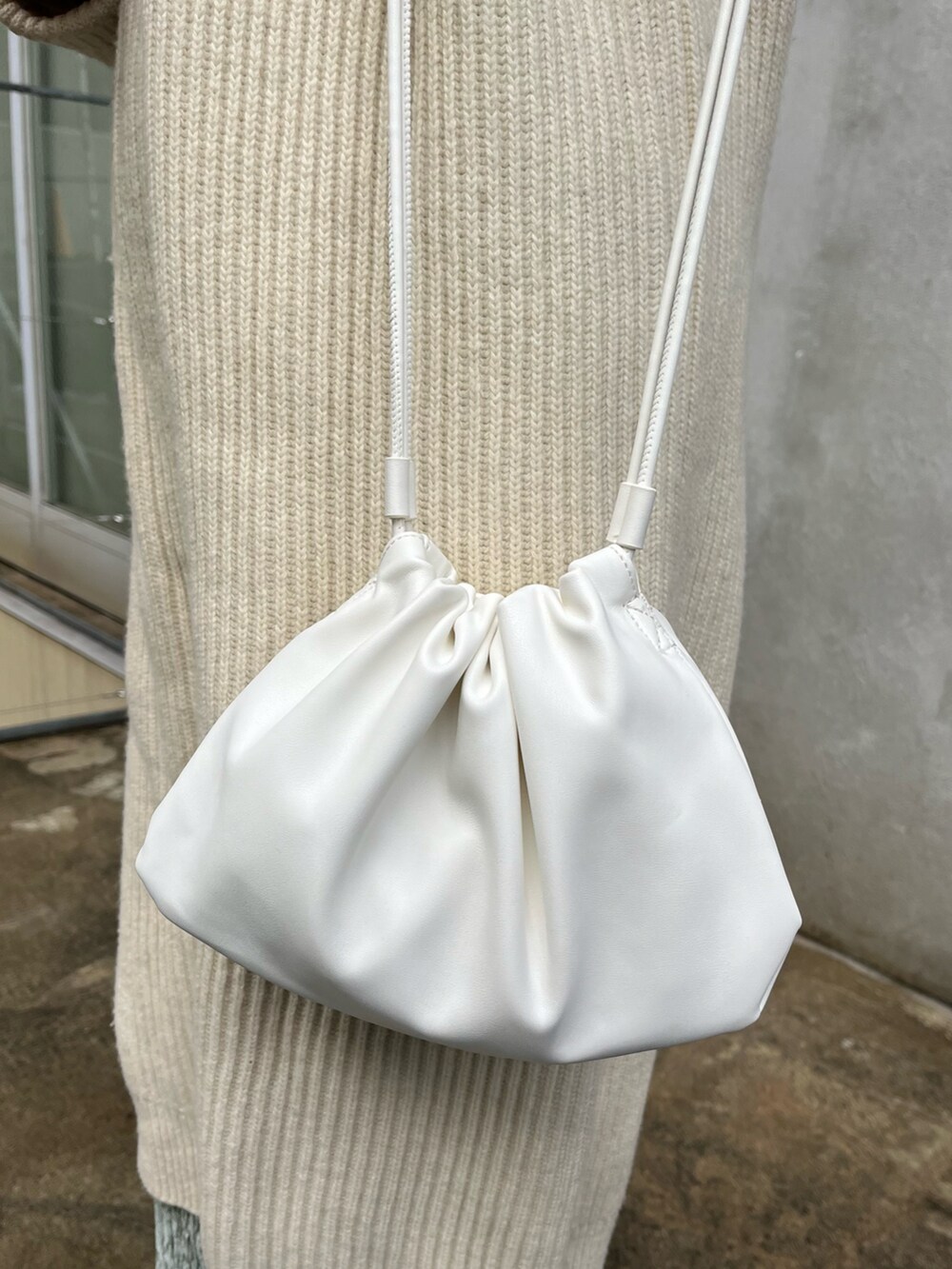 ホワイト系のショルダーバッグ、ホワイト系のスニーカー、ベージュ系のニット/セーターを着用したレディースの冬コーディネートの2枚目の写真