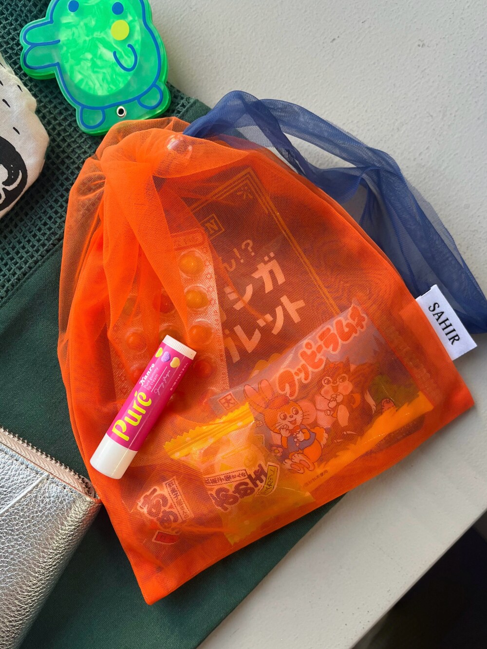 シルバー系の財布、オレンジ系のポーチ、ブルー系のキーホルダーを着用したレディースの春コーディネートの2枚目の写真