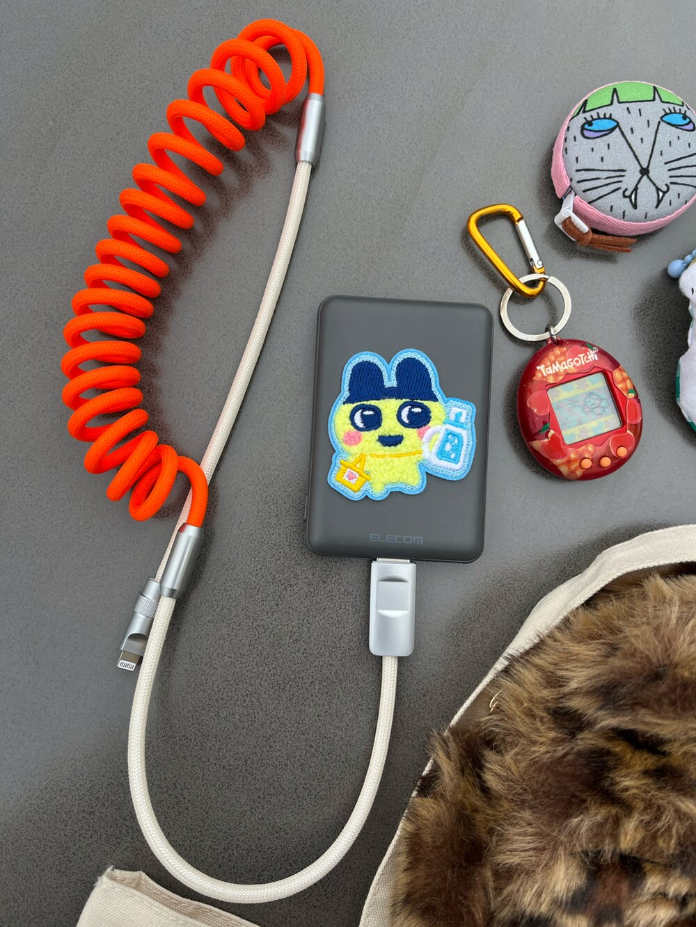 オレンジ系のスマホグッズ、ブルー系のハンドケア/ハンドクリーム、オレンジ系のキーホルダーを着用したレディースの春コーディネートの3枚目の写真