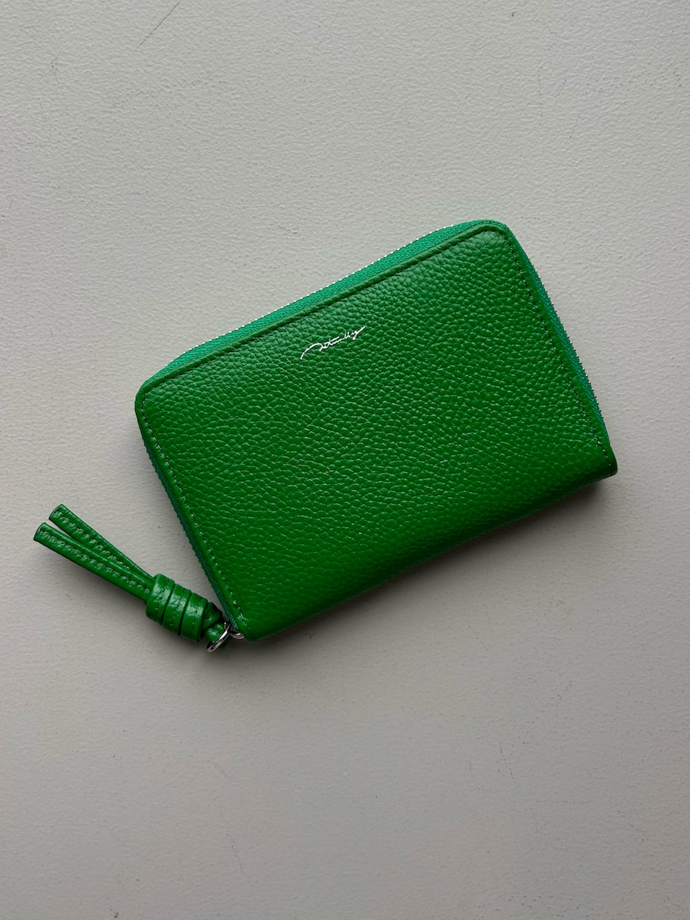 グリーン系の財布、グレー系のポーチ、ホワイト系のチャームを着用したレディースの春コーディネートの2枚目の写真